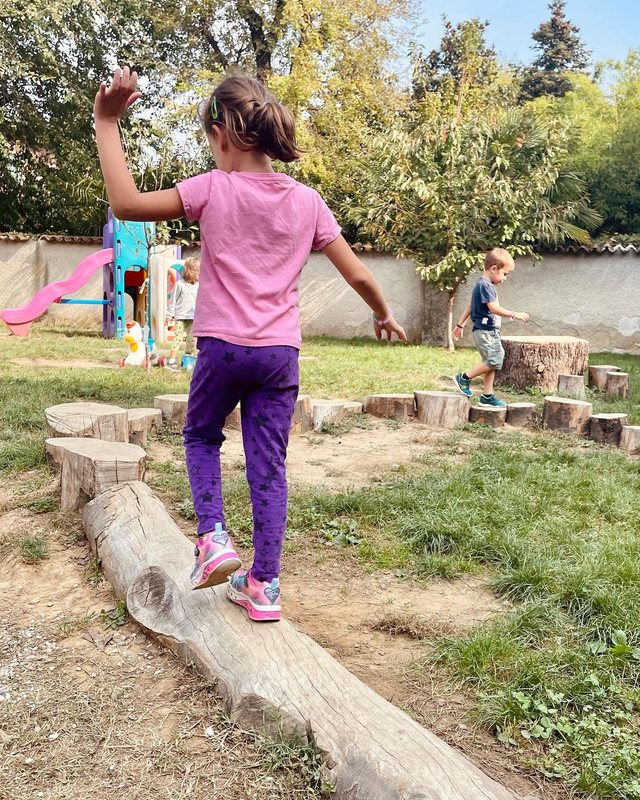 Una bambina cammina in equilibrio su un tronco nel giardino