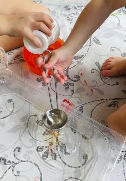 Mani di bambini giocano con l’acqua e un mestolo